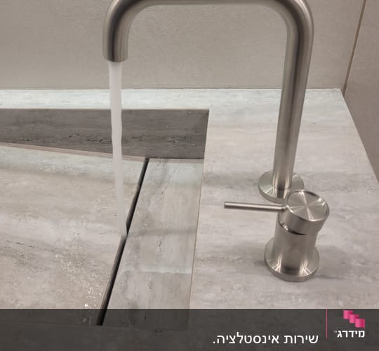 ברז נירוסטה עם מים זורמים בכיור אבן